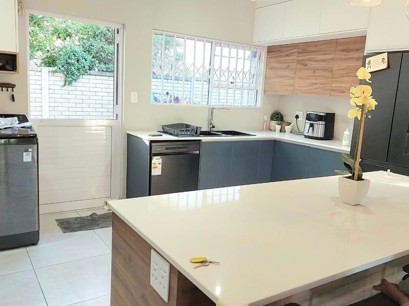 Modern kitchen featuring a central island with quartz countertops, sleek cabinetry, and direct access to the exterior through a secure door.