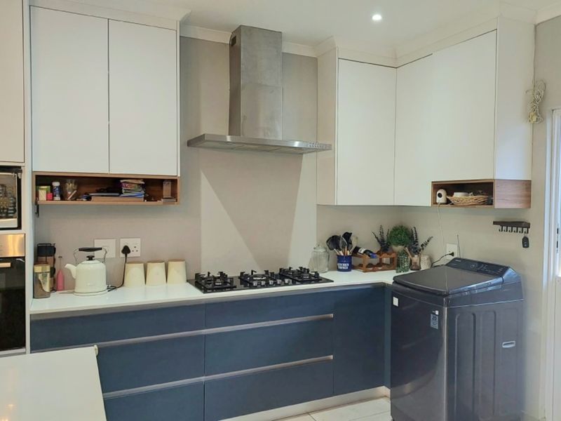 Modern kitchen featuring two-tone cabinetry, stone countertops, a gas hob with stainless steel extractor, and integrated appliances.