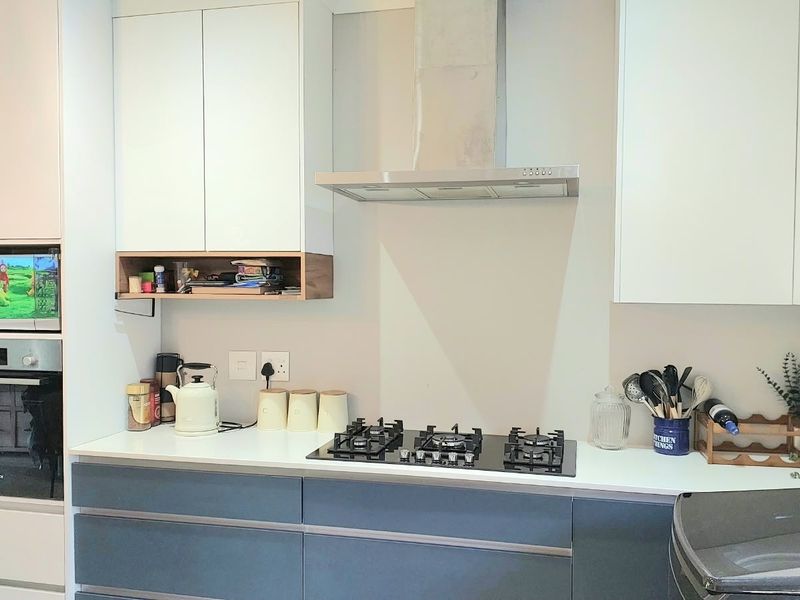 Modern kitchen featuring sleek white and grey cabinetry, stone countertops, a built-in oven, microwave, and a stainless steel extractor fan over a gas hob.
