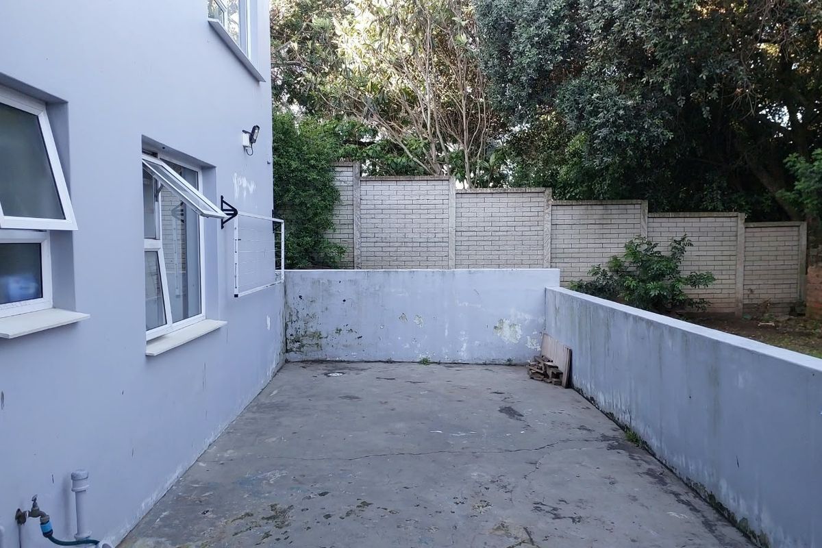 A private rear courtyard featuring a concrete patio, boundary walls, and an external water point, offering potential for outdoor living space improvement.