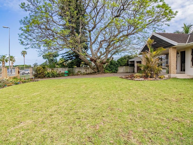 A well-maintained front exterior featuring a spacious lawn, mature trees, paved driveway, and a brick-accented facade with a tiled roof.