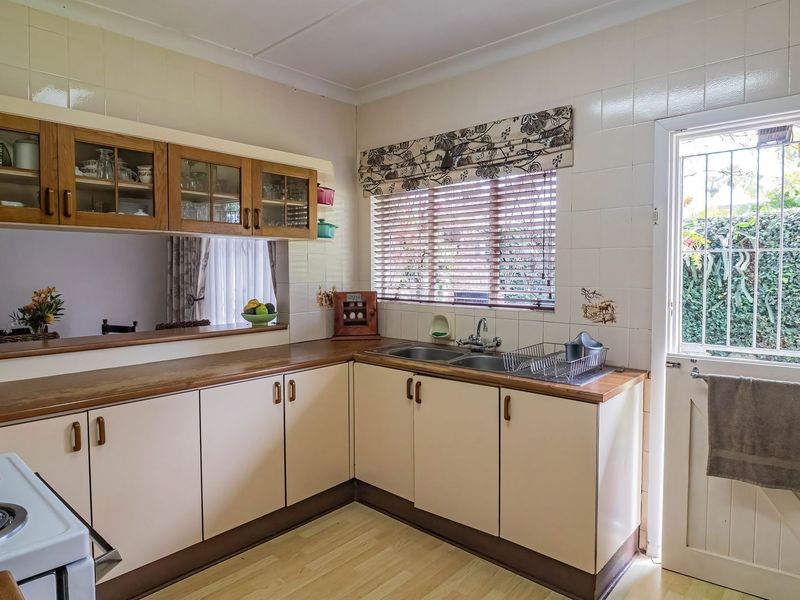 A functional kitchen featuring laminate countertops, double bowl sink, tiled splashback, and ample storage cabinetry with direct access to the exterior.