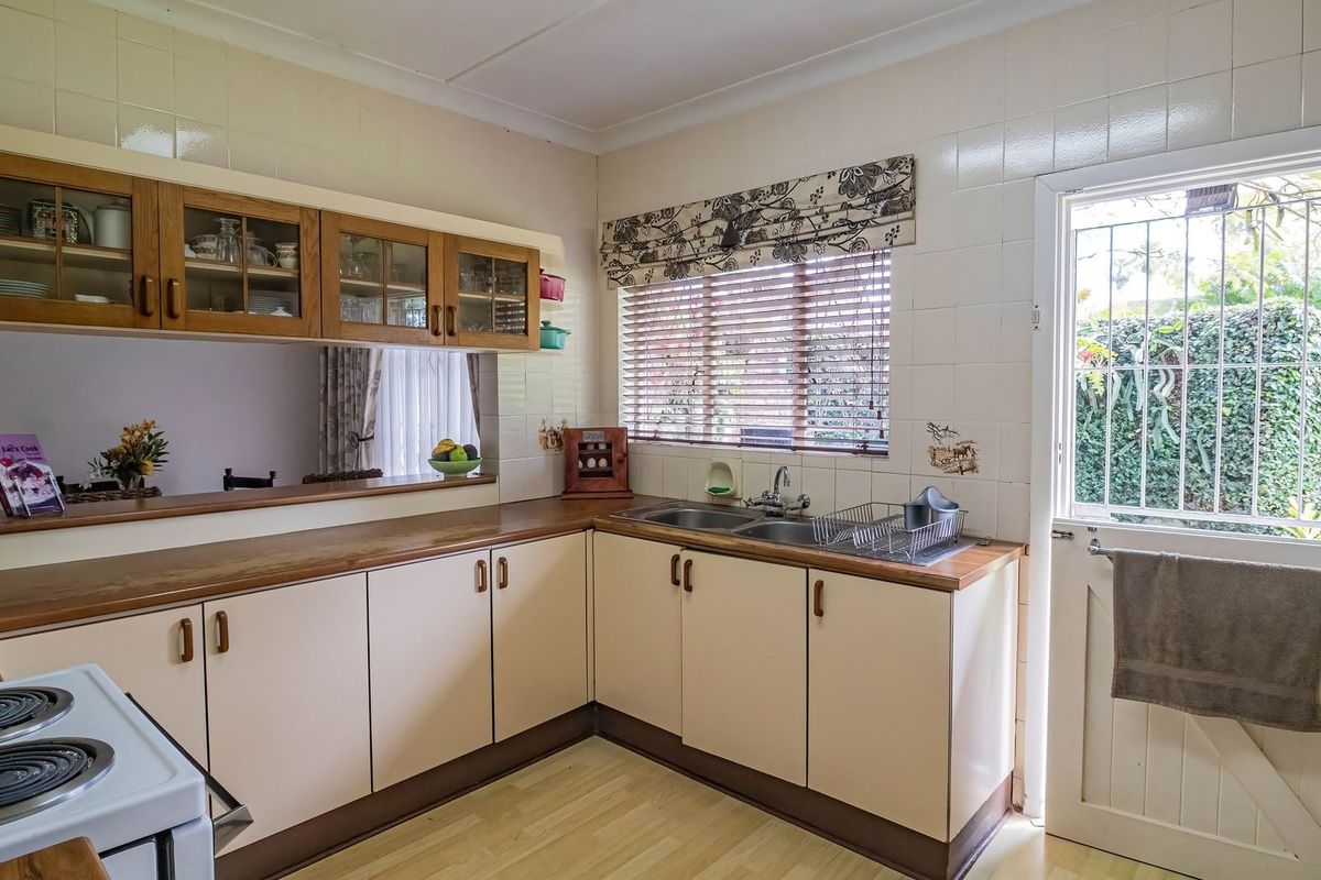A functional kitchen featuring laminate countertops, double bowl sink, tiled splashback, and ample storage cabinetry with direct access to the exterior.
