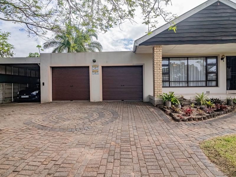 Front view of the property featuring a paved driveway, double garage, attached carport, and a well-maintained landscaped garden bed.