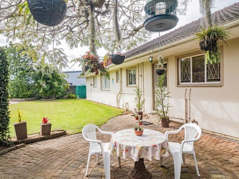 A well-maintained rear exterior featuring a brick-paved patio area, established lawn, and secure window fixtures, providing a pleasant outdoor living space.