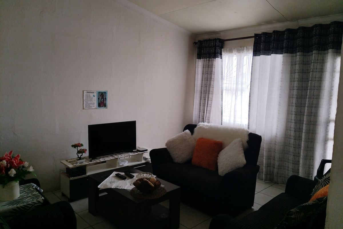 A living room featuring tiled flooring and a window fitted with security bars, offering a functional space with potential for cosmetic updates.