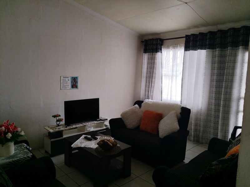 A living room featuring tiled flooring and a window fitted with security bars, offering a functional space with potential for cosmetic updates.