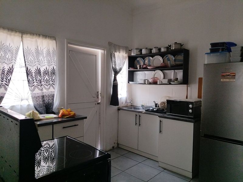 A functional kitchen featuring built-in cabinetry, open shelving, a sink, and tiled flooring, providing a practical workspace for daily meal preparation.
