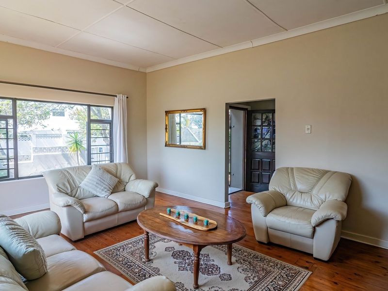 A bright living room featuring polished timber flooring, a large window providing natural light, and a classic timber door with stained glass accents.
