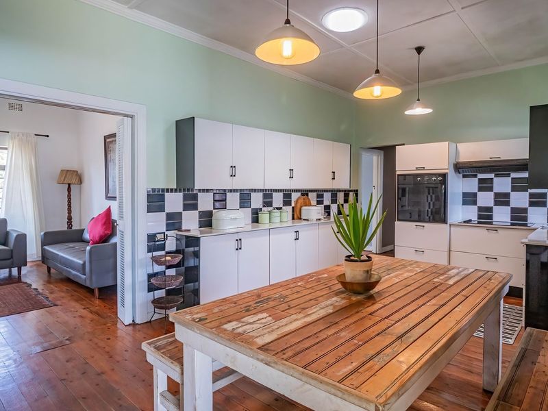 A functional kitchen featuring white cabinetry, a distinctive checkerboard tile backsplash, built-in oven, extractor fan, and warm hardwood flooring with overhead pendant lighting.