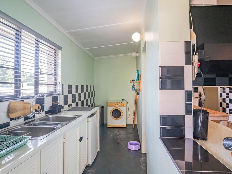 Functional scullery area featuring a double stainless steel sink, tiled splashback, and built-in cabinetry with ample counter space.
