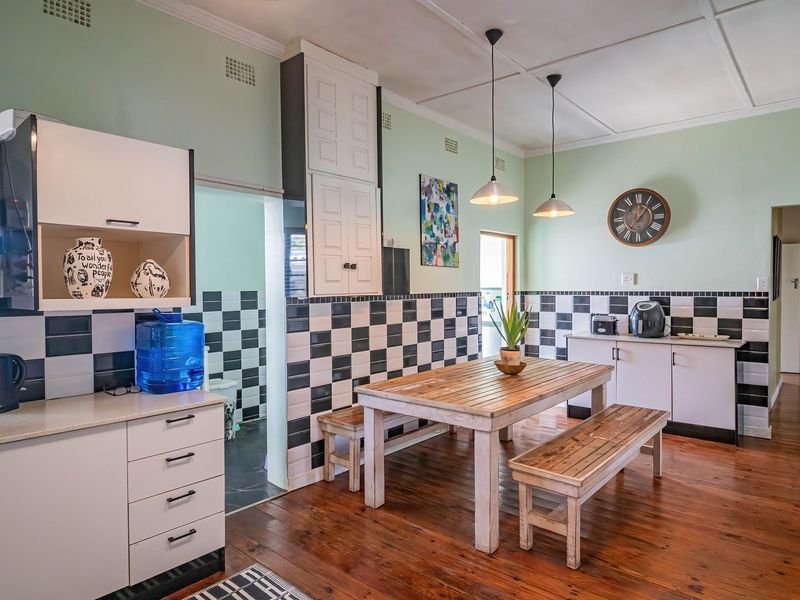 Open plan kitchen and dining area featuring timber flooring, checkerboard wall tiling, built-in cabinetry, and pendant lighting.
