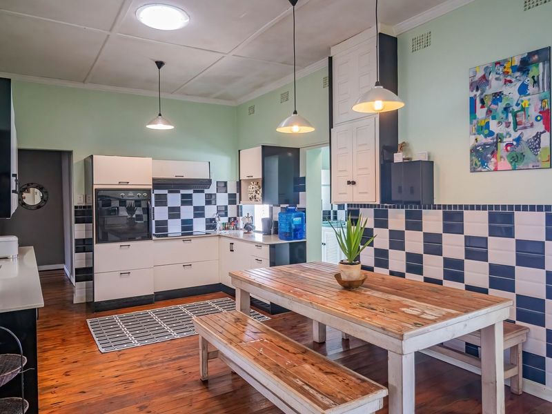 A kitchen featuring hardwood floors, checkerboard tiled splashbacks, built-in oven, extractor fan, and ample cabinetry with a dedicated dining area.
