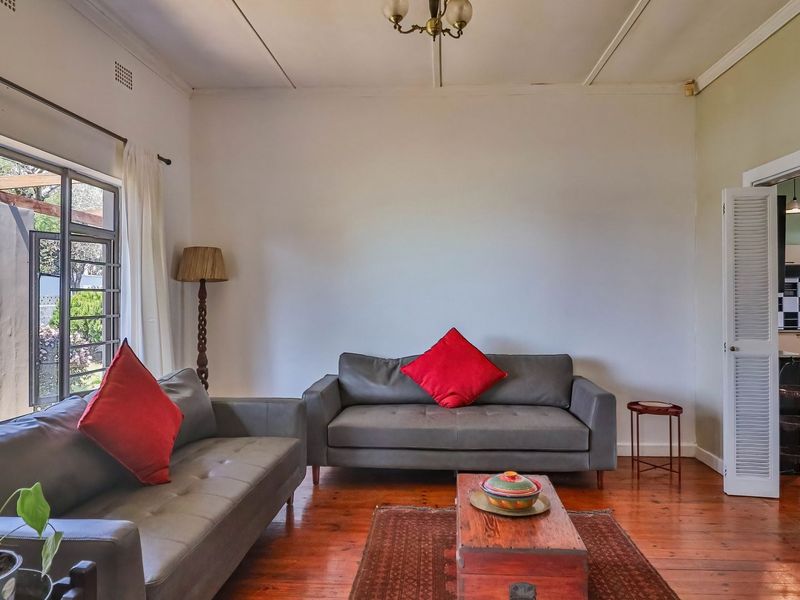 A bright living room featuring polished hardwood flooring, a large sliding glass door providing natural light, and access to an adjacent kitchen area.