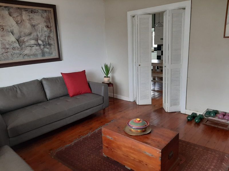 A living room featuring polished hardwood flooring and white louvered bi-fold doors leading to an adjacent space.
