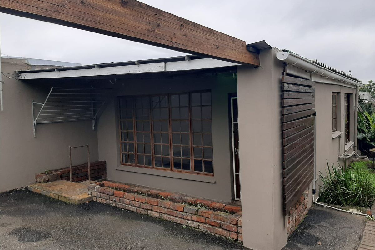 Rear exterior view featuring a covered patio area with a timber beam, brick planter, and privacy screen, showing signs of weathering.