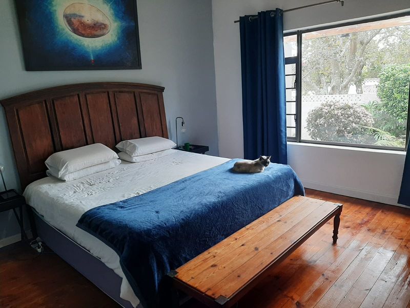 A well-lit bedroom featuring polished hardwood flooring and a large window overlooking the garden area.