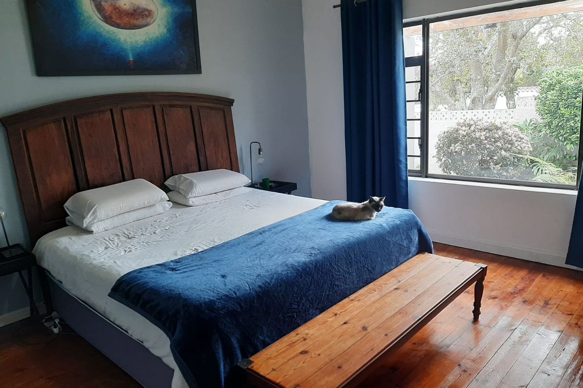 A well-lit bedroom featuring polished hardwood flooring and a large window overlooking the garden area.