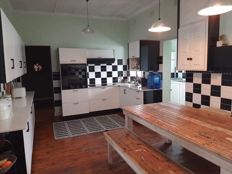 Spacious kitchen featuring a black and white checkerboard splashback, built-in oven and hob, ample cabinetry, and warm timber flooring.