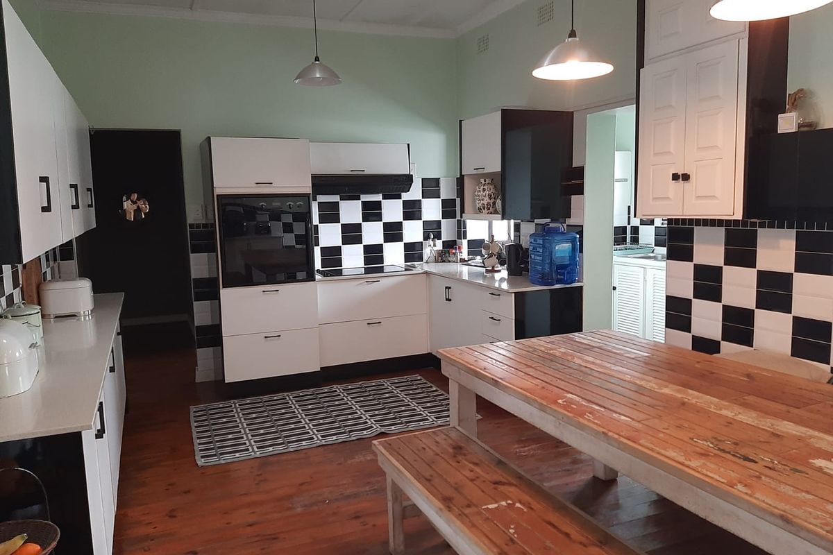 Spacious kitchen featuring a black and white checkerboard splashback, built-in oven and hob, ample cabinetry, and warm timber flooring.