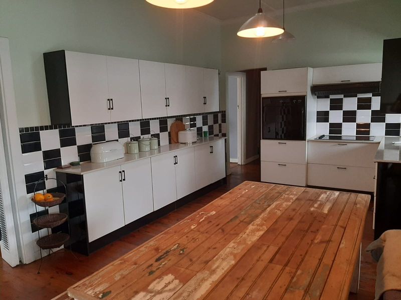 A functional kitchen featuring white cabinetry, a black and white checkered tiled splashback, built-in oven, and hardwood flooring.