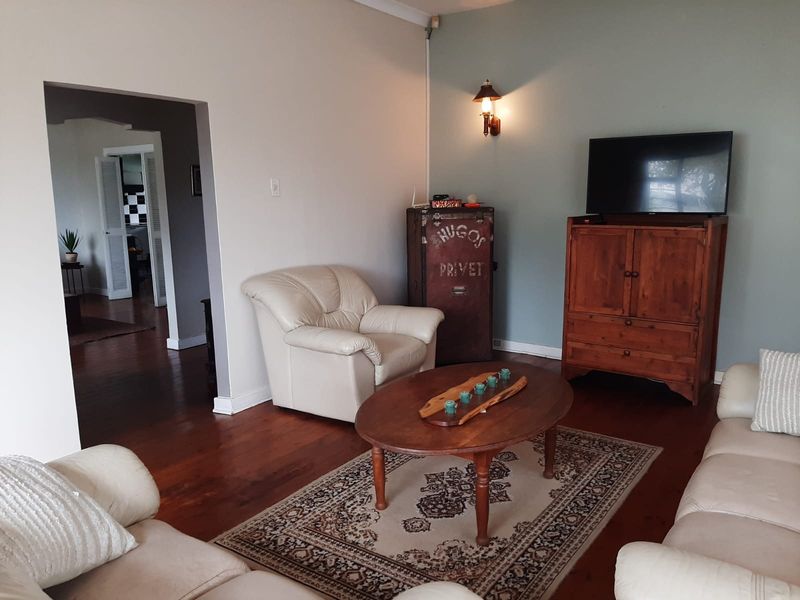 A comfortable living room featuring polished hardwood flooring, a decorative wall sconce, and coving, with an open transition to the adjacent room.