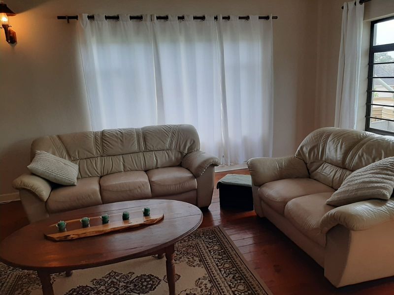 A comfortable living room featuring hardwood flooring, a wall-mounted light fixture, and large windows dressed with curtains.