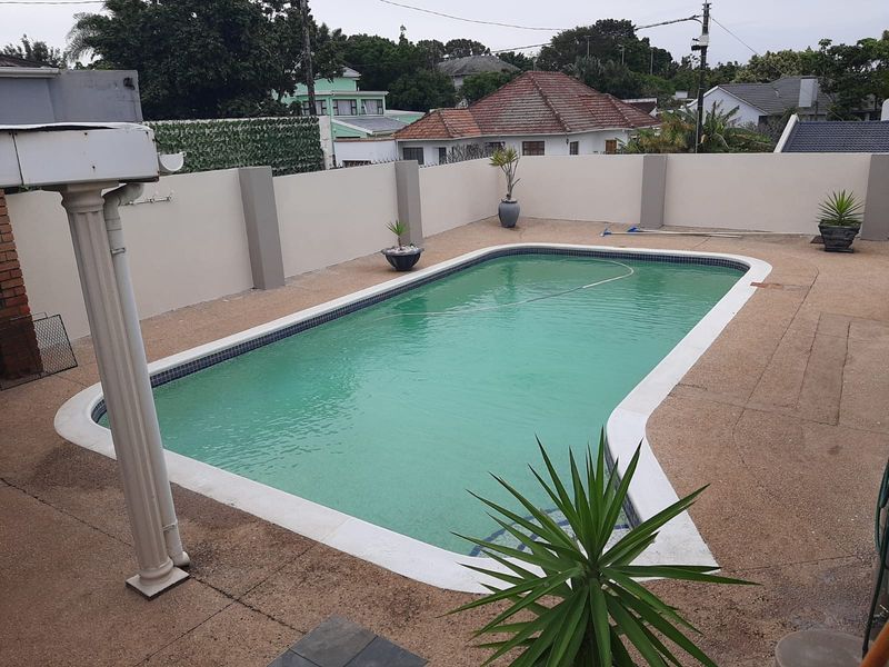 Outdoor swimming pool area featuring aggregate paving and a high perimeter wall for privacy.