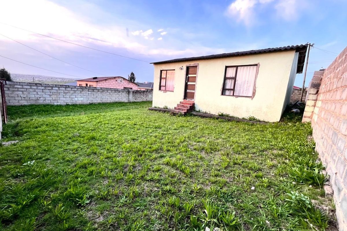 Rear view of a detached house featuring a large grass yard enclosed by concrete block boundary walls.