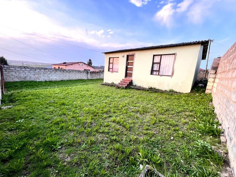 Rear view of a detached house featuring a large grass yard enclosed by concrete block boundary walls.