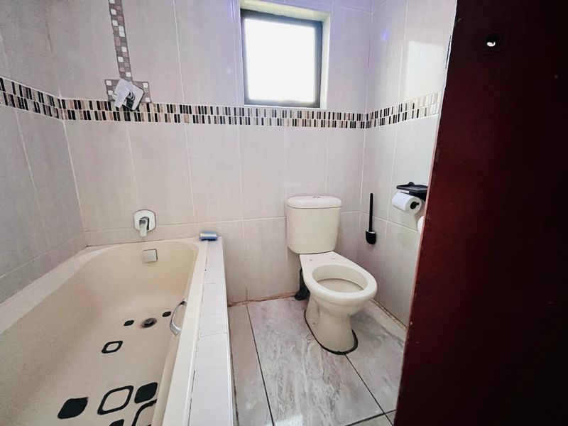 A functional bathroom featuring a bathtub, toilet, and tiled finishes, offering a neutral base ready for modern updates.