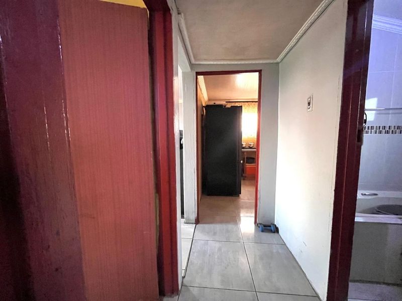 A narrow interior hallway with tiled flooring and painted door frames, providing access to adjacent rooms including a kitchen and bathroom area.