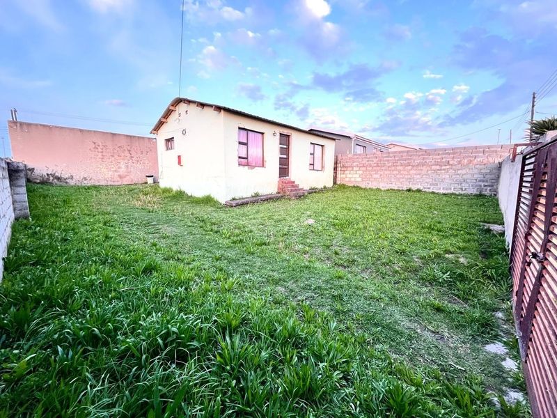 Rear view of a detached house featuring a large grassed yard, perimeter boundary walls, and a metal access gate.