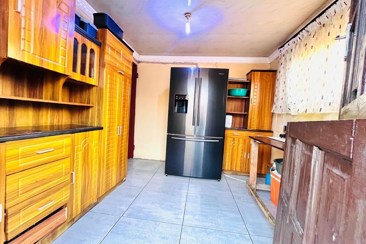 A kitchen featuring wooden cabinetry and tiled flooring, showing signs of wear and requiring cosmetic updates to improve the overall finish.