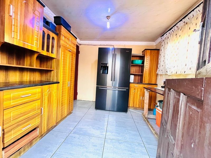 A kitchen featuring wooden cabinetry and tiled flooring, showing signs of wear and requiring cosmetic updates to improve the overall finish.