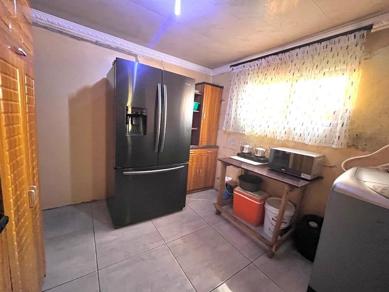 A functional kitchen area featuring tiled flooring and built-in cabinetry, currently requiring wall repairs and cosmetic updates to improve the overall finish.