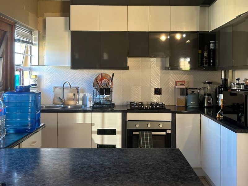 Modern kitchen featuring two-tone cabinetry, gas hob, built-in oven, and dark laminate countertops with a textured tiled backsplash.