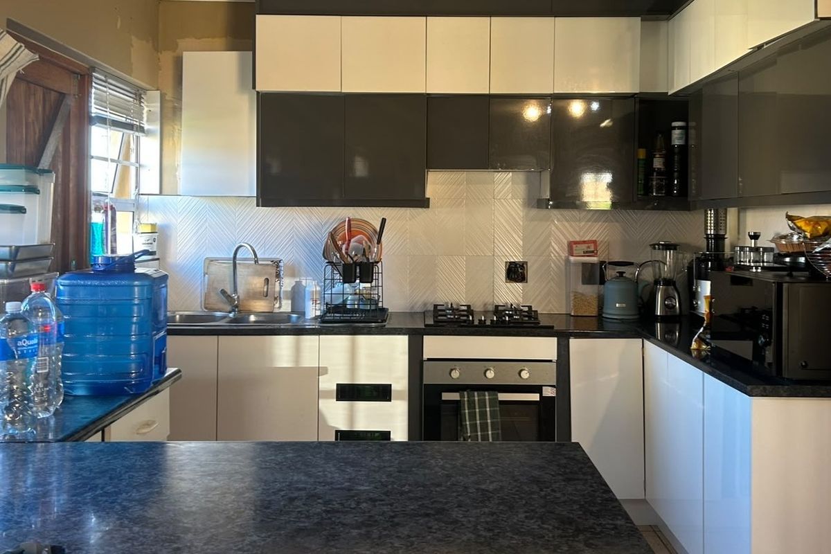 Modern kitchen featuring two-tone cabinetry, gas hob, built-in oven, and dark laminate countertops with a textured tiled backsplash.