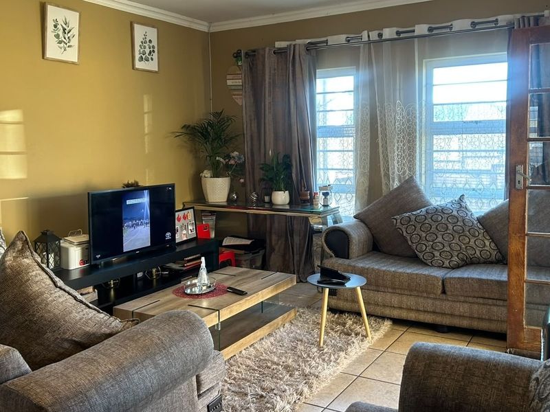 A comfortable living room featuring tiled flooring, a classic french door, and windows fitted with security bars, offering a functional and lived-in space.