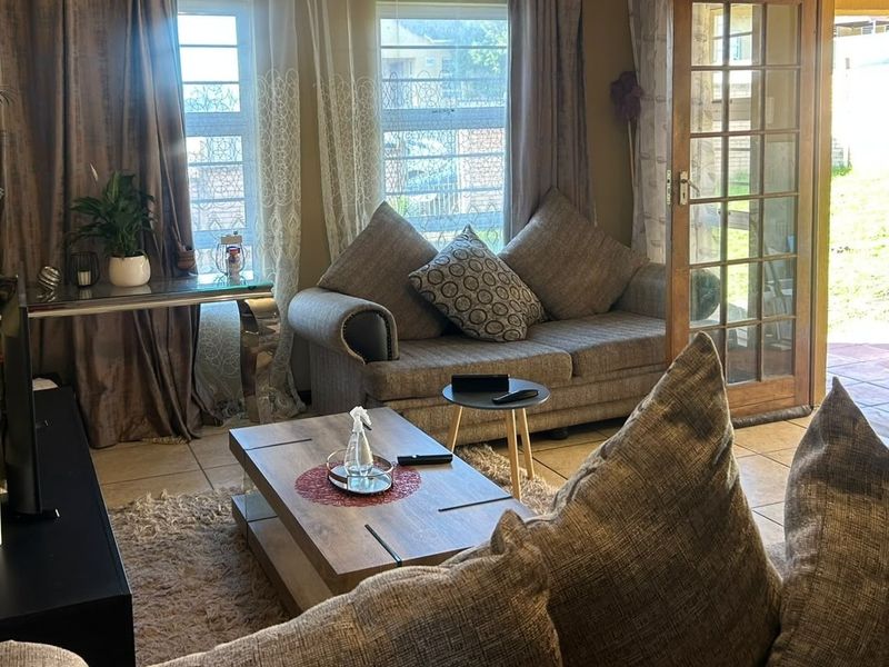 A comfortable living room featuring tiled flooring, large windows for natural light, and direct access to the outdoor area through classic french doors.