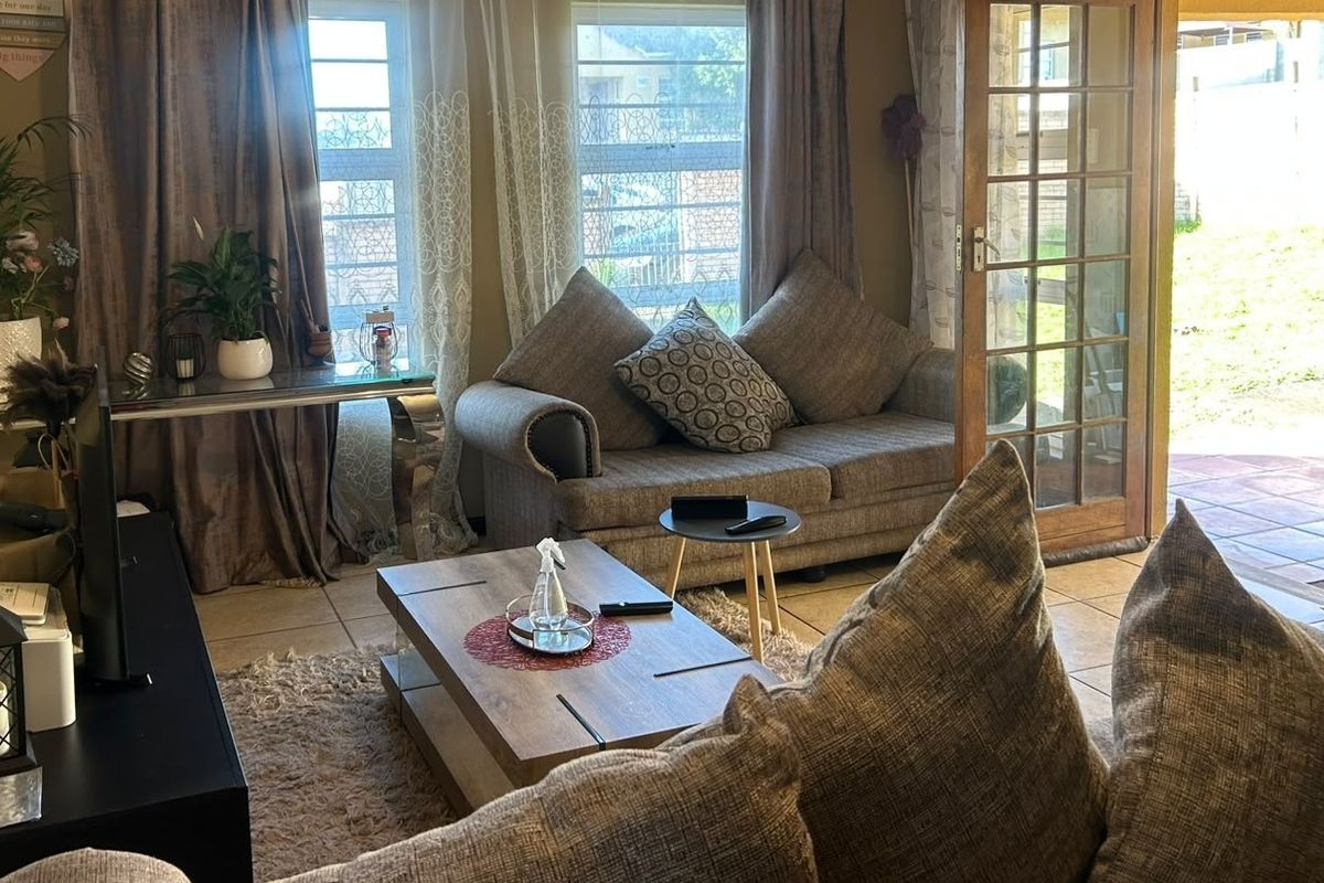 A comfortable living room featuring tiled flooring, large windows for natural light, and direct access to the outdoor area through classic french doors.