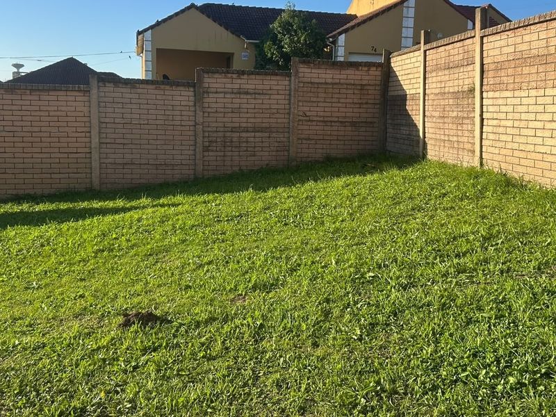 A private garden area enclosed by a brick boundary wall and metal gate, featuring a grass lawn.