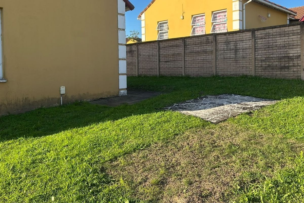 Rear garden area featuring a lawn, brick boundary wall, and concrete apron along the townhouse exterior wall.
