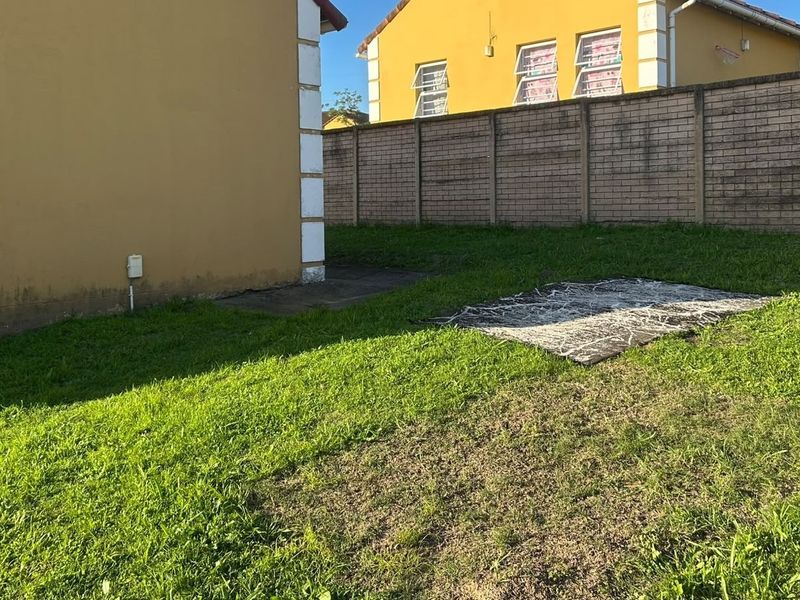 Rear garden area featuring a lawn, brick boundary wall, and concrete apron along the townhouse exterior wall.