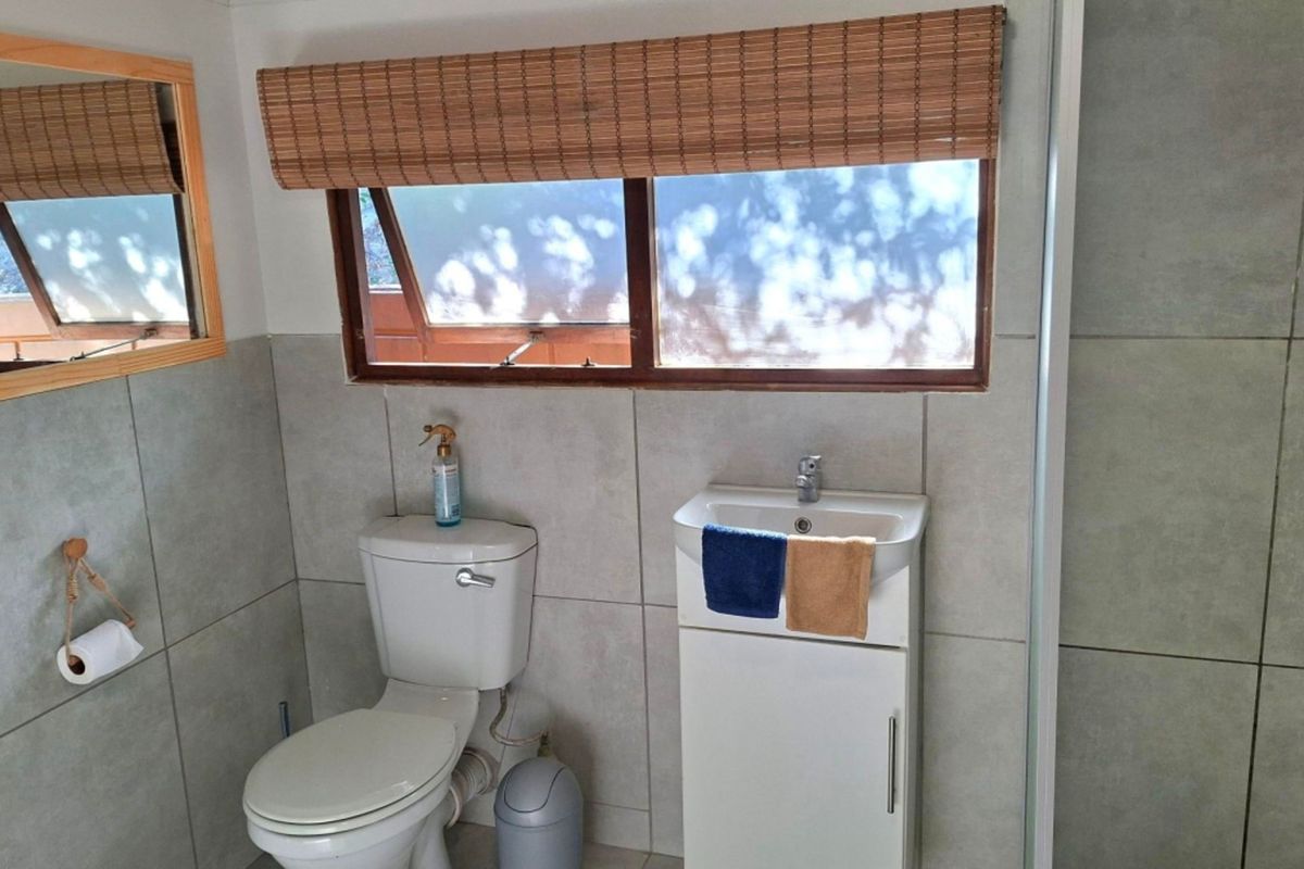 A functional bathroom featuring tiled walls, a vanity basin, and a toilet, with natural light provided by a window with a bamboo blind.