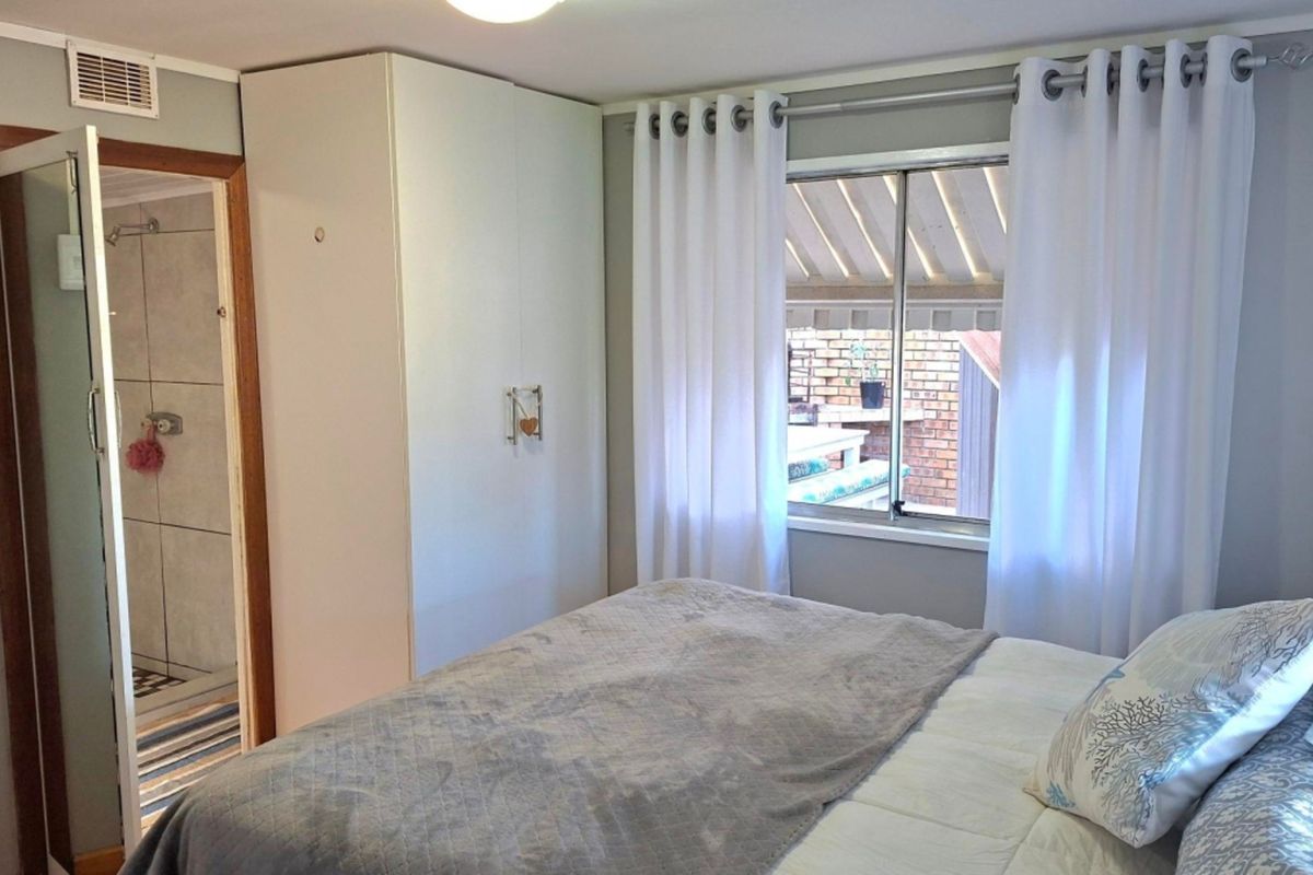 A functional bedroom featuring a built-in wardrobe, natural light from a sliding window, and direct access to an en-suite bathroom.
