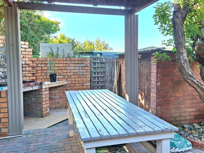 Outdoor patio area featuring a brick built-in braai, covered by a timber pergola, set within a paved garden space.