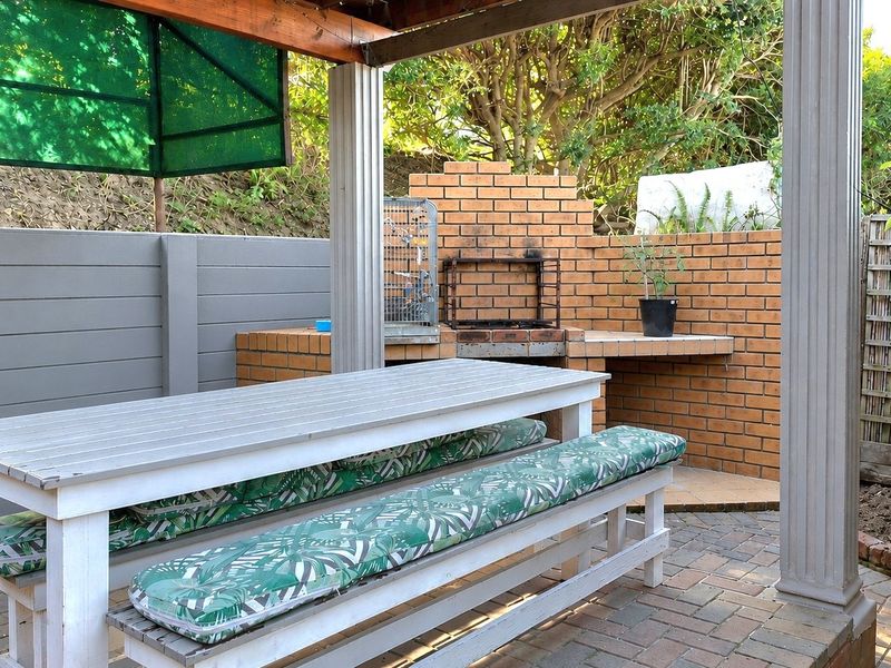 Covered outdoor patio area featuring a built-in brick braai, paved flooring, and a timber pergola structure, ideal for alfresco dining and entertaining.