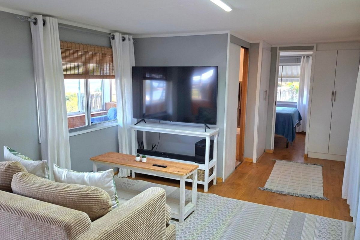 A well-maintained living room featuring timber flooring, neutral wall tones, and built-in storage, with a seamless transition to an adjacent bedroom area.