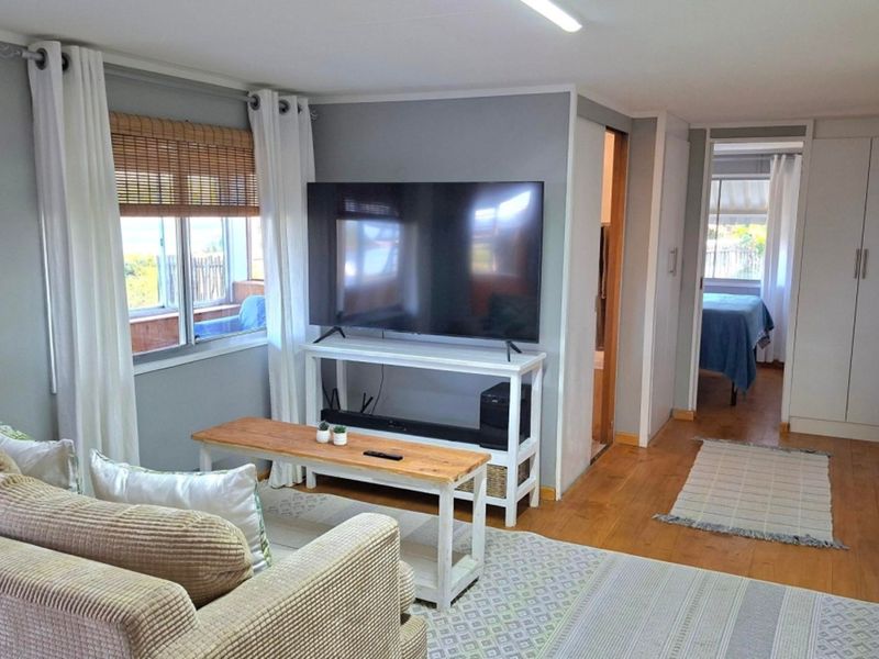 A well-maintained living room featuring timber flooring, neutral wall tones, and built-in storage, with a seamless transition to an adjacent bedroom area.
